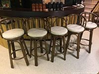 Front view of all five bamboo style swivel barstools with fabric seats lined up in a row.