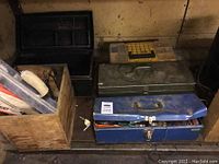 Two blue metal tool chests and a wooden box, one chest partially open revealing contents