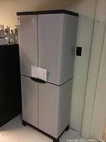 Closed front view of the plastic two-door utility cabinet showing textured doors in light grey and black top and base accents.