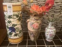 Photo showing all three vases in a row with floral and leaf decorative motifs, including artificial flowers in two vases.