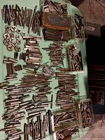 Wide shot showing the assorted drill bits, lathe tools, and threading dies spread out on a green surface with plastic containers included