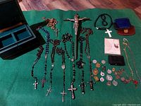 Overview of many antique rosaries, crucifixes, medals, and a black display box on green cloth.