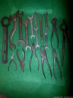 Full set of 17 antique tools spread on green cloth including wrenches, pliers, cutters, and grabbers with various shapes and sizes.