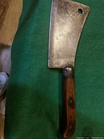 Photo of one antique handmade meat cleaver with metal blade and wooden handle on green fabric background