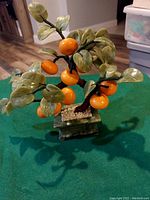 Jade bonsai orange tree with green leaves and orange fruit in marble base on green cloth.