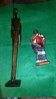 Full view of both African collectible items on green cloth background, showing the warrior statue and the wax lady figure together.