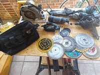 Full view of the Dewalt 7.25" circular saw, RotoZip saw, Dremel Saw Max, Makita sheetrock tool, black carrying case, and assorted cutting blades spread on a wooden surface.
