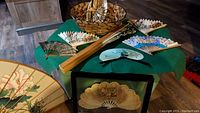 Overview of the collection showing various hand fans and two woven baskets on a green table with framed fan in front