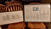 Two framed historical plans side by side on wooden chairs, showing full size and framing of maps and prints.