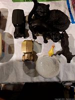Top-down view showing all items in lot including black cast iron cats, bull/cow, cars, ceramic bird bath with yellow bird, and two oil lamp holders