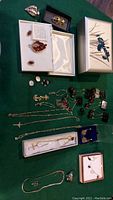 Full view of jewelry assortment including earrings, pins, chains, pendants, and a music box on green felt surface.
