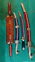 Three Indian knives and fork sets laid flat showing carved wooden sheaths and fabric sheaths in red, blue, and black.