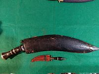 Top view of large Gurkha Kukri knife and small accompanying knife laid on a green cloth