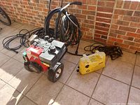Tecumseh 8.0 HP gas-powered pressure washer with attached hoses and yellow Karcher electric pressure washer on tiled floor against brick wall