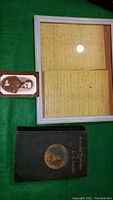 Photo of the framed original letter and the photo postcard alongside the memoir book on a green surface.
