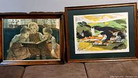 Two framed art prints displayed side-by-side on a surface: left is The 3 Girls Reading by Walther Firle depicting three girls reading a book, right is The Misty Landscape by Reginald Landers showing a colorful village landscape.