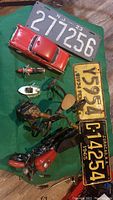 View of three vintage license plates and nine collectible model vehicles and ornaments arranged on a green cloth.