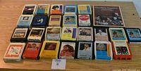 25 assorted 8 track tapes laid out on a wood surface showing colorful cases and visible labels with various artists.