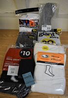 Photo showing various unopened packs of men's socks including Athletic Works white crew socks, black diabetic socks, Giant Value pack, and grey Acten shoe inserts.