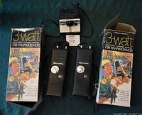 Two Realistic 3-watt CB transceivers in their original boxes with a Polaroid camera between them on a dark surface.