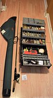 Overview showing the fishing rod inside the Bushline bag alongside the open Blackhawk 6-section tackle box filled with fishing lures and accessories.