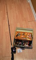 Full view of Silstar fishing rod with foam handle and mounted reel next to Rebel 510 tackle box on wood floor.