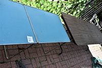 Blue and brown foldable tables side by side on brick patio, showing overall condition and general appearance.