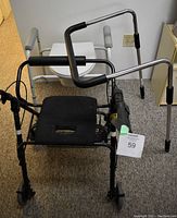 Photo of two walkers and one toilet support assist. The black folding walker features a padded seat and front wheels. The white walker is a basic model with padded armrests. The white toilet support assist has a seat and padded armrests and sits on the carpet.