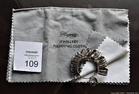 Jewelry polishing cloth laid flat with ring sizer placed on one side and auction tag.