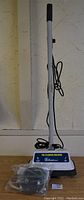 Full view of the Koblenz floor buffer standing upright with the power cord wrapped around the handle. Bag with scrubbing pads placed in front of the base.