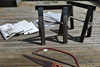 Photo showing two wooden saw horses, several folded white tarps, and two saws on a wooden deck