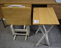 Set of 4 portable TV tables showing wooden tops and foldable white legs, with 1 table set up and 3 stacked