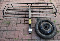 Overview of cargo rack laid flat next to spare tire on brick pavers