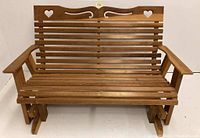 Front view of wooden roll back porch glider bench with slatted seat and back featuring heart and scroll cutouts