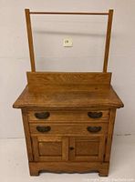 Front view of antique oak commode washstand showing two metal-handled drawers and double-door cabinet beneath with attached towel rod.