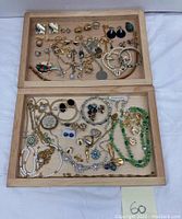 Wide view of two wooden trays with assorted costume jewelry including necklaces, earrings, rings, and bracelets in various metal tones and styles.