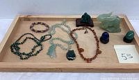 Wide view of all gemstone jewelry and ornaments displayed on a wooden tray, showing necklaces, pendants, and carved figures