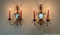 Pair of gold-tone mid-century wall sconces with mirrored backs, floral decoration, hanging crystal prisms, and red candles, wall mounted and lit