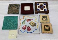 Seven vintage Art Deco decorative tiles arranged on a white surface, showing abstract, animal, and fruit motifs.
