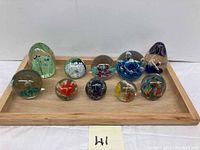 Photo of all 10 vintage art glass paperweights arranged on wooden tray showing range of colors and shapes