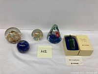 Five art glass paperweights arranged in a row showing different internal designs, with one boxed glass bird figurine included