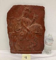 Front view of the terracotta wall plaque with Guanyin on horseback showing full relief detail and size comparison with water bottle.