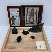 Overview of framed artworks and five carved figurines arranged on wooden tray.