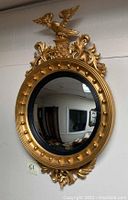 Front view of entire oval vintage mirror with gold painted frame and eagle motif on top