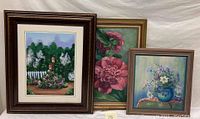 Three framed oil paintings displayed together: one landscape and two floral still lifes.