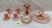 Full view of all pink Depression glassware pieces grouped together, showing candle holders, nut/candy dish, comport, and serving tray with center handle.