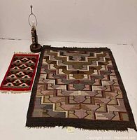 Photo showing all three items together: a wooden totem lamp, a large handwoven wool blanket with geometric bird design, and a smaller colorful handwoven tapestry.