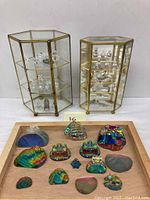 Overview showing two brass and glass hexagonal display cabinets and wooden tray with assorted iridescent paperweights.
