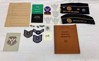 Top view of multiple Air Force patches, pins, two American Legion hats, booklets, and brochures arranged on a white surface.