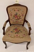 Front view of vintage chair showing needlework upholstery with floral design on seat and back, and carved wood frame and legs.